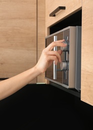 Photo of Young woman adjusting modern microwave oven in kitchen, closeup