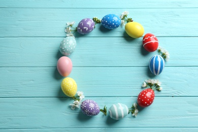 Photo of Frame made of painted Easter eggs and flowers on wooden background, flat lay. Space for text