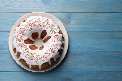 Photo of Glazed Easter cake with sprinkles on blue wooden table, top view. Space for text