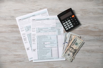 Photo of Payroll. Tax return forms, calculator and dollar banknotes on wooden table, flat lay