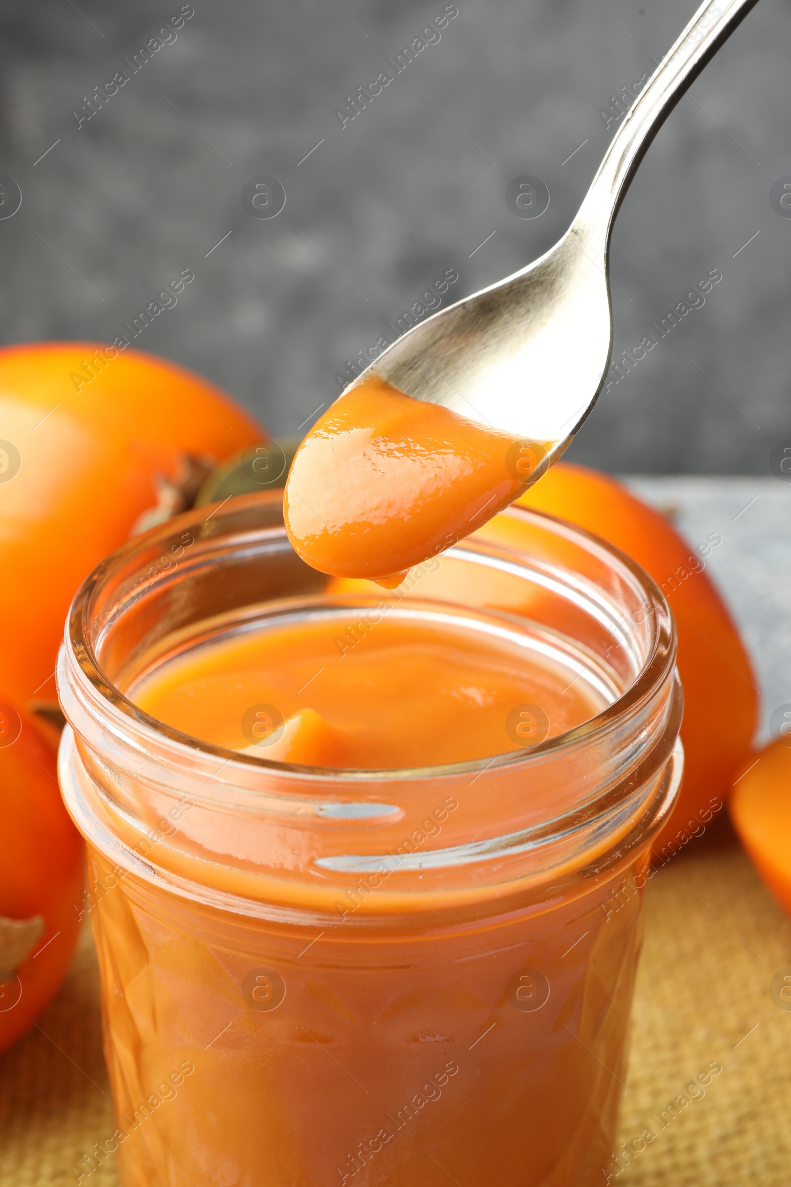 Photo of Taking delicious persimmon jam with spoon from glass jar on table, closeup