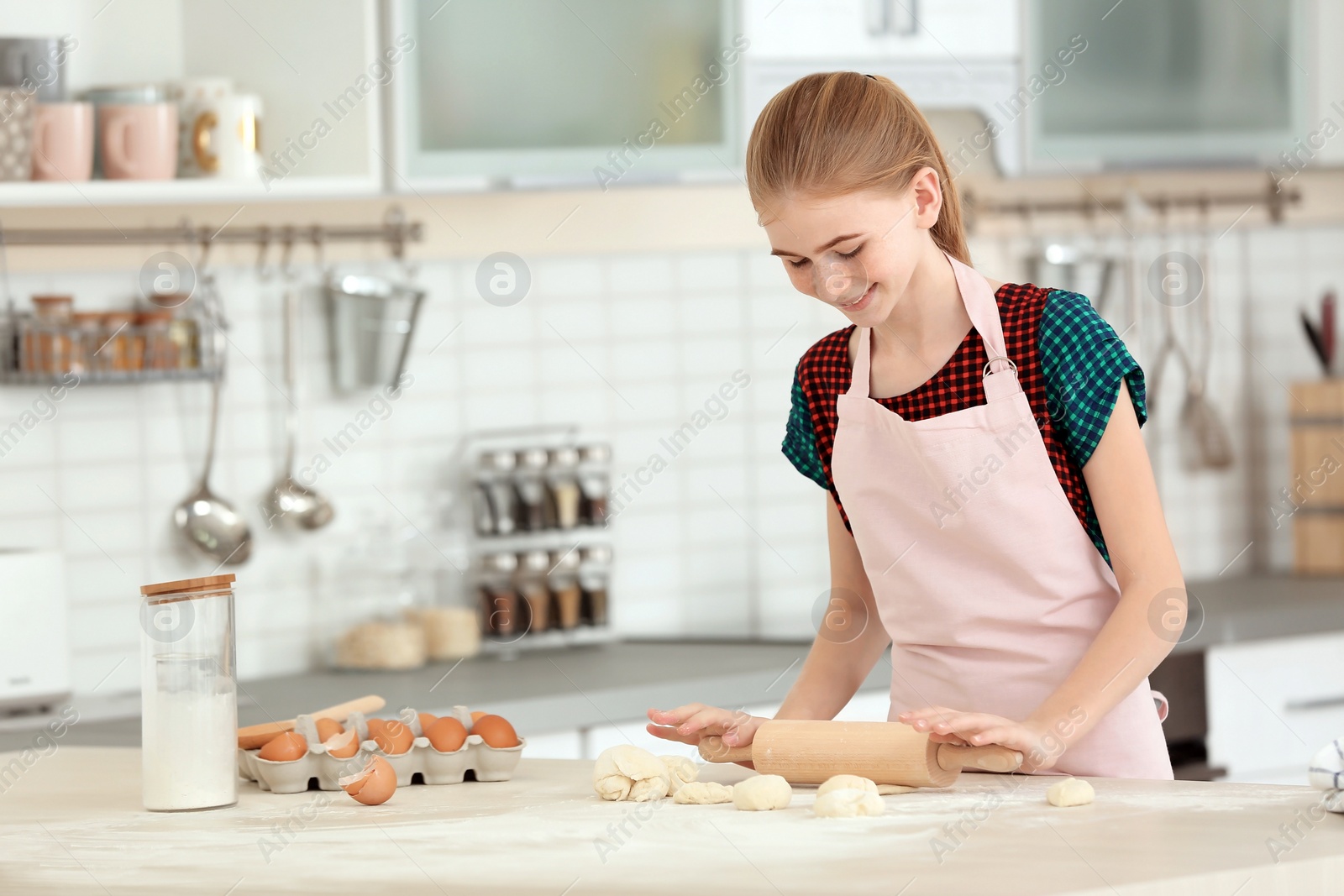 Photo of Teenage girl rolling dough on table in kitchen