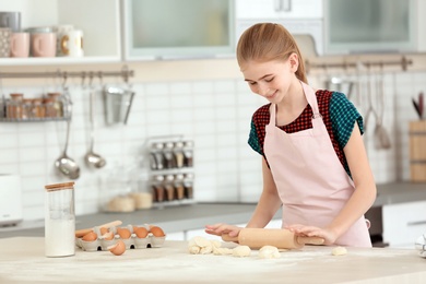 Photo of Teenage girl rolling dough on table in kitchen