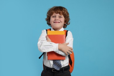 Photo of Happy schoolboy with backpack and books on light blue background