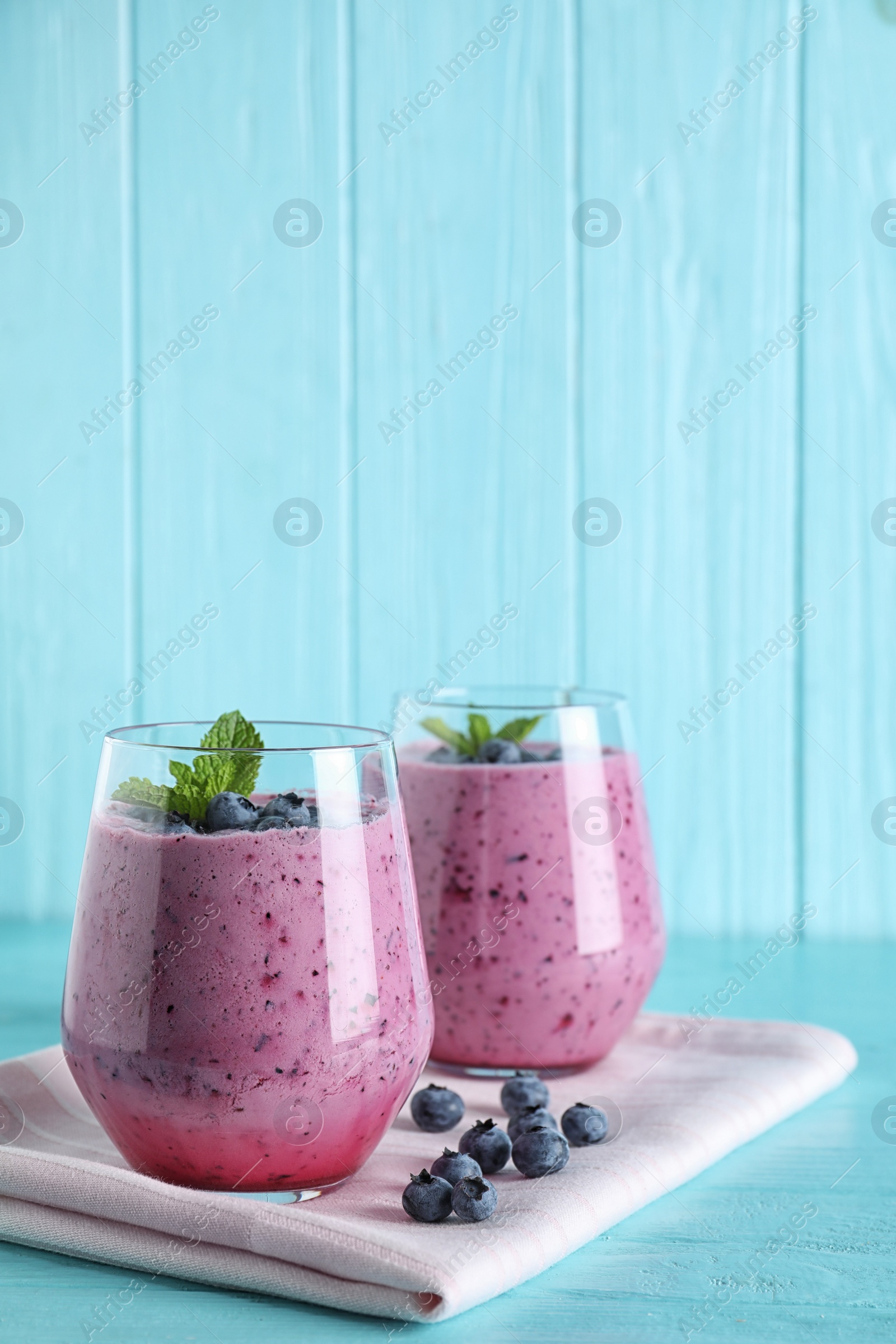 Photo of Glasses of tasty blueberry smoothie and fabric on light blue wooden table, space for text