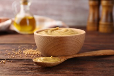 Photo of Bowl and spoon with tasty mustard sauce on wooden table, closeup