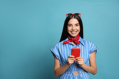 Photo of Fashionable young woman in stylish outfit with bandana using smartphone on light blue background, space for text