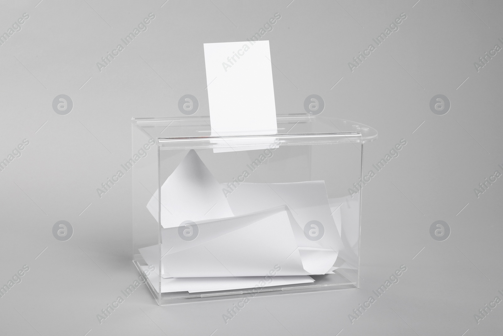 Photo of Ballot box with votes on light grey background. Election time