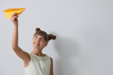 Cute little girl playing with paper plane on light grey background. Space for text