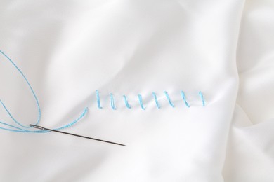 Sewing needle with thread and stitches on white cloth, top view