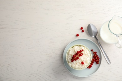 Photo of Creamy rice pudding with red currant in bowl served on white wooden table, top view. Space for text