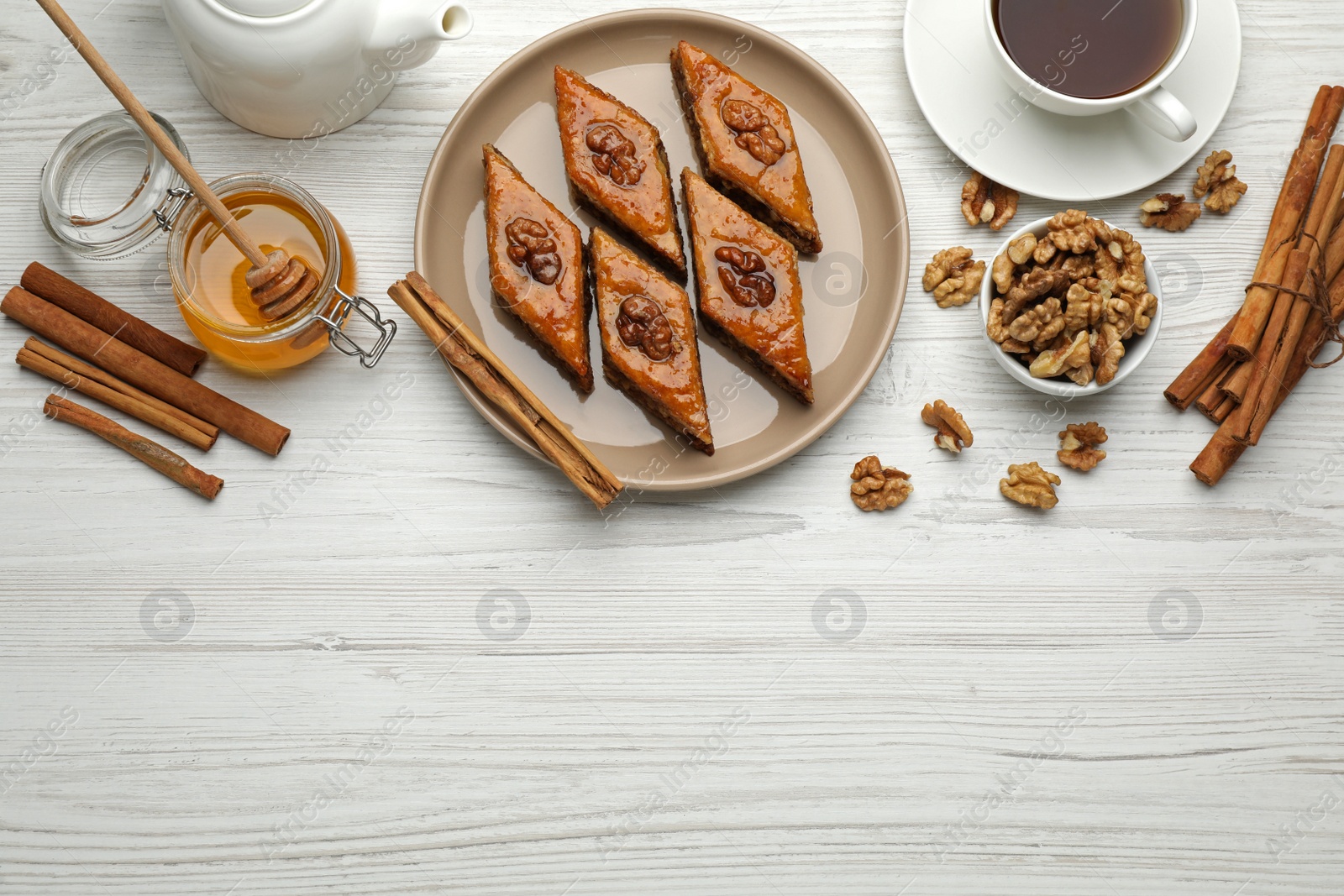 Photo of Delicious sweet baklava with walnuts, honey, cinnamon and hot tea on white wooden table, flat lay. Space for text