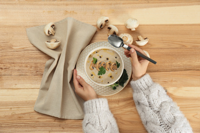 Photo of Woman eating fresh mushroom soup at wooden table, top view