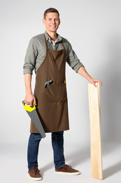 Handsome carpenter with wooden planks and hand saw on light grey background