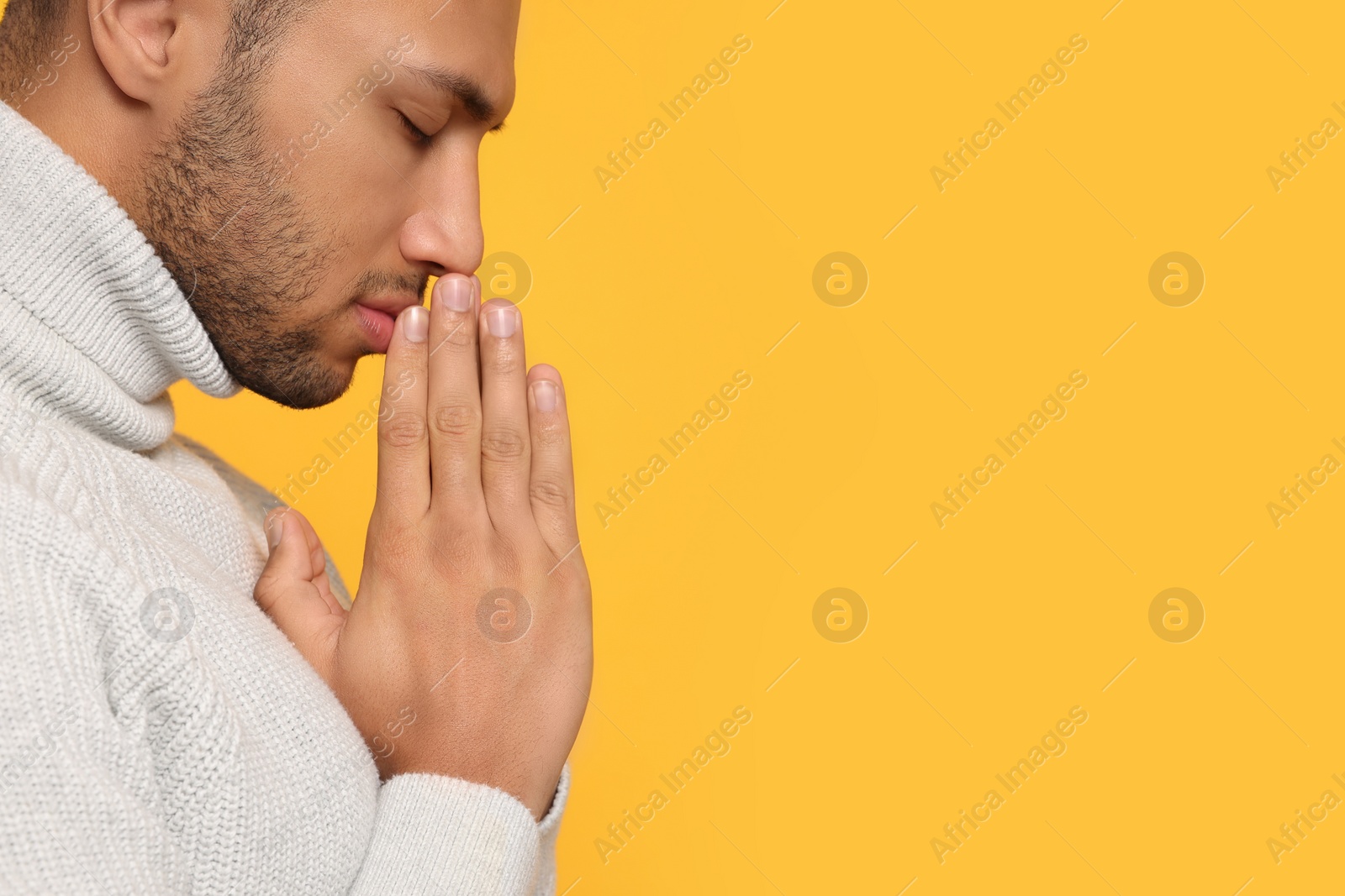 Photo of African American man with clasped hands praying to God on orange background, closeup. Space for text