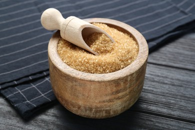 Photo of Brown sugar in bowl and scoop on black wooden table, closeup