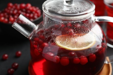 Photo of Tasty hot cranberry tea with lemon and fresh berries in teapot on black table, closeup