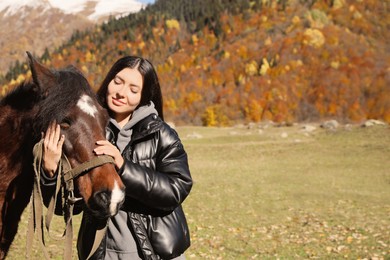 Photo of Young woman stroking horse in mountains on sunny day, space for text. Beautiful pet