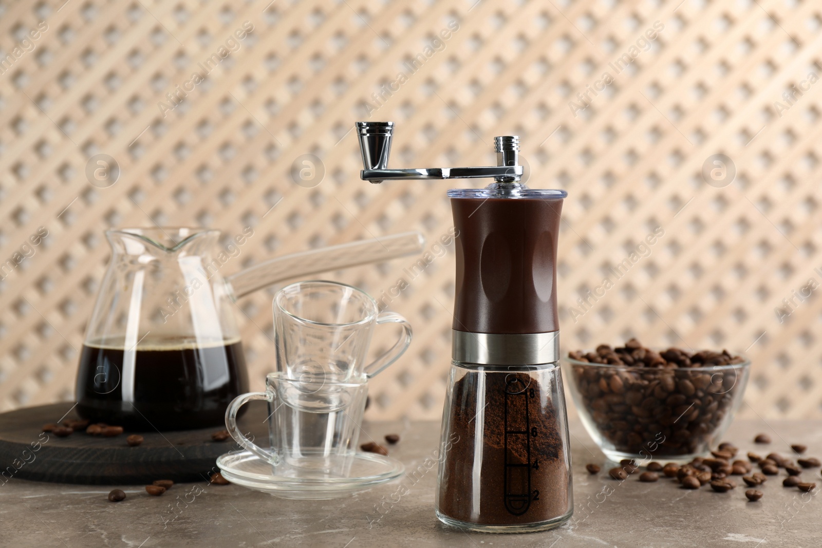 Photo of Manual coffee grinder with powder, beans and drink on grey table