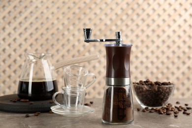 Manual coffee grinder with powder, beans and drink on grey table