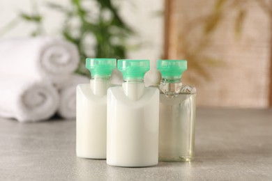 Mini bottles of cosmetic products on light grey table against blurred background