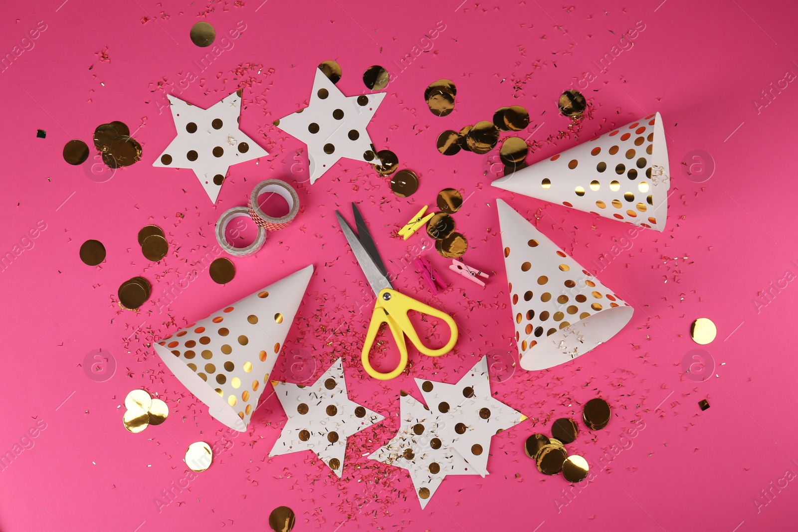 Photo of Party hats with confetti, paper stars, scissors and tapes on pink background, flat lay. Handmade decorations
