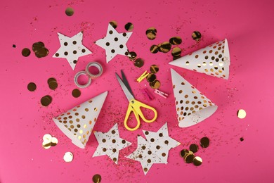 Party hats with confetti, paper stars, scissors and tapes on pink background, flat lay. Handmade decorations