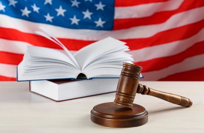 Photo of Judge's gavel and books on white wooden table against American flag