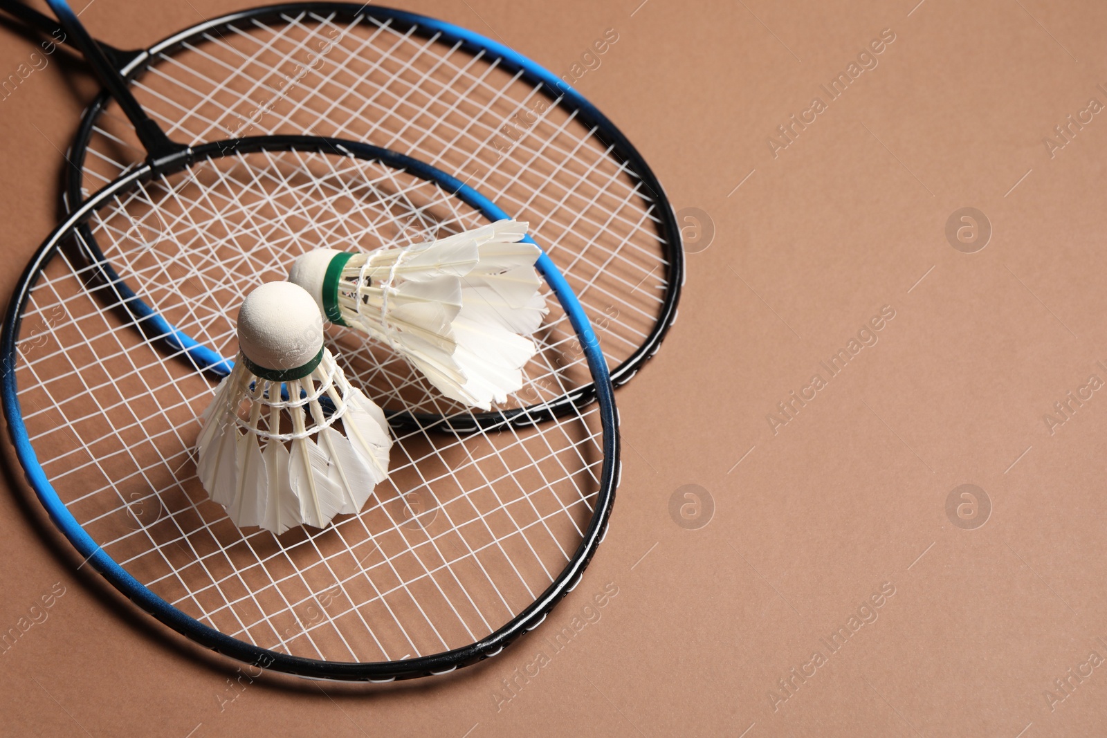 Photo of Feather badminton shuttlecocks and rackets on brown background, space for text