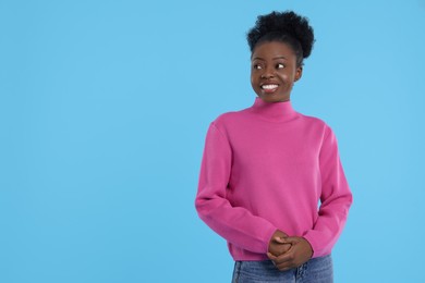Portrait of happy young woman on light blue background. Space for text