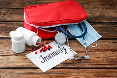 Photo of Paper sheet with word Immunity and first aid kit on wooden table