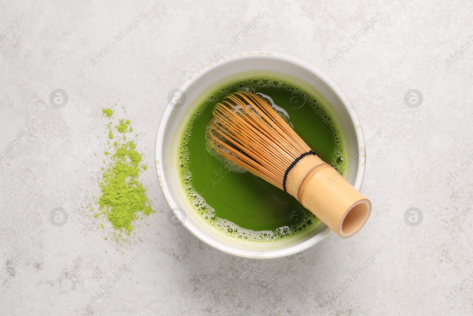 Photo of Bowl of fresh matcha tea with bamboo whisk and powder on light table, flat lay