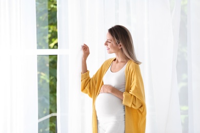 Photo of Happy pregnant woman standing near window at home