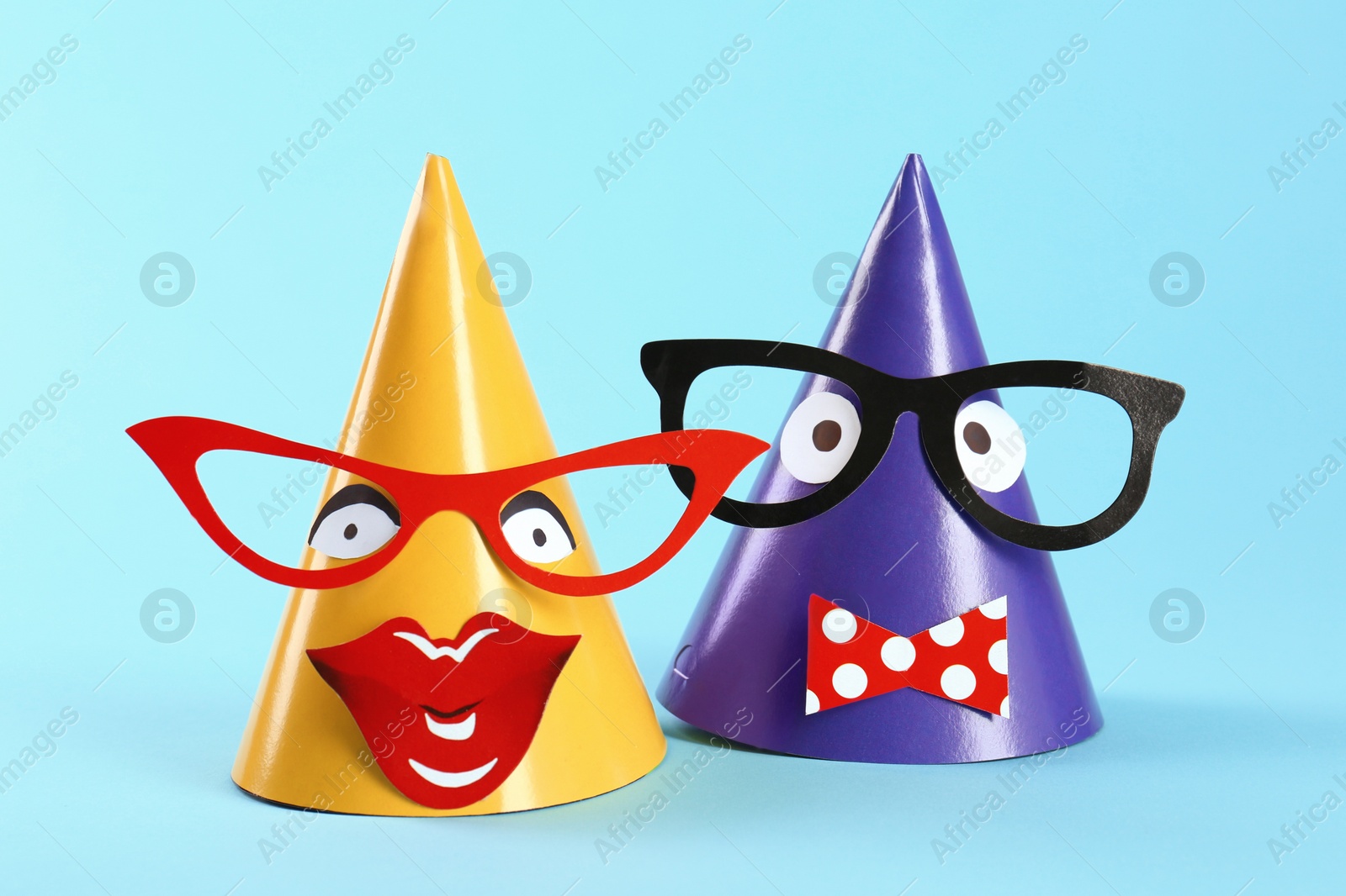 Photo of Handmade party hats with funny faces on light blue background
