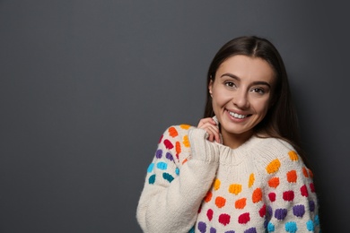 Beautiful young woman in warm sweater on dark background. Space for text