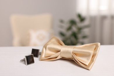 Photo of Stylish beige bow tie and cufflinks on white wooden table, closeup