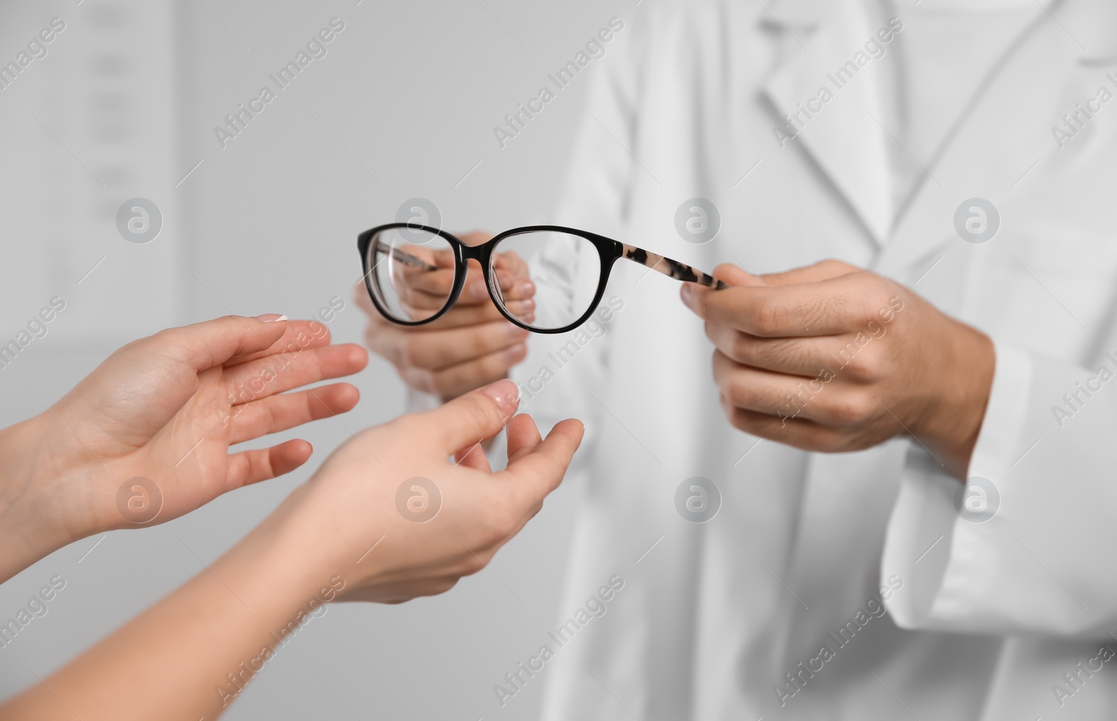 Photo of Male ophthalmologist helping woman choose glasses in clinic, closeup