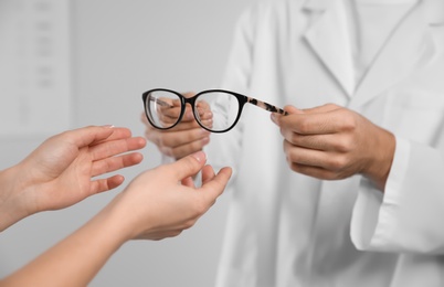 Male ophthalmologist helping woman choose glasses in clinic, closeup