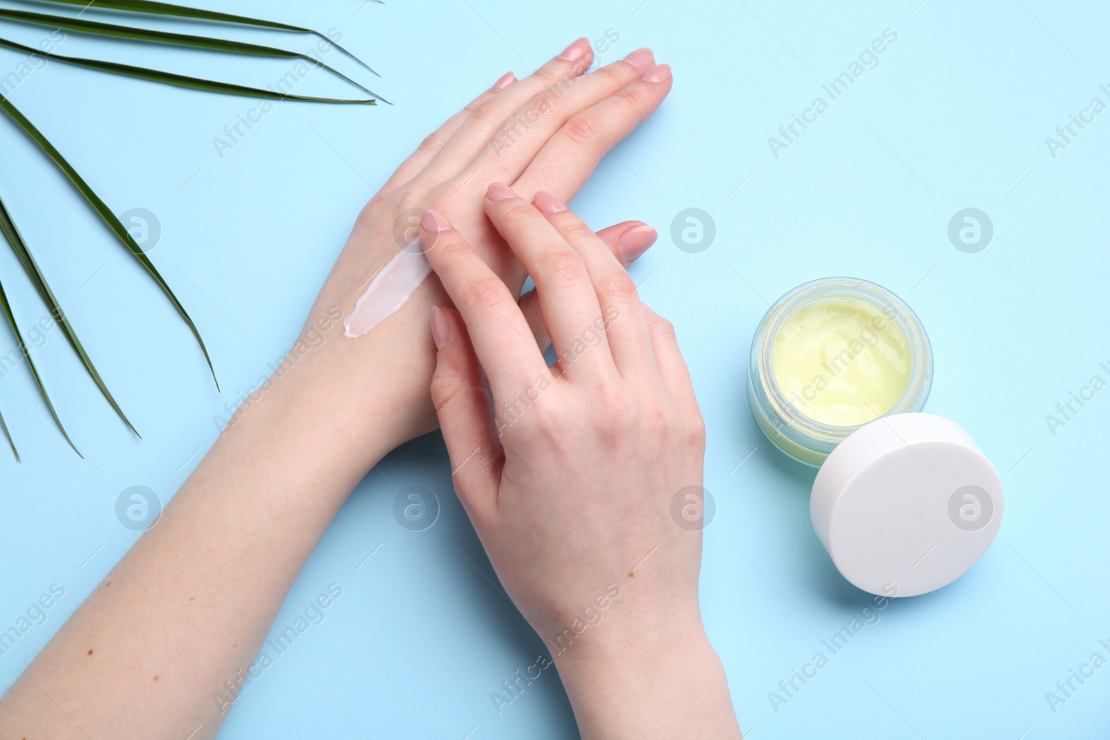 Photo of Woman applying hand cream on light blue background, top view