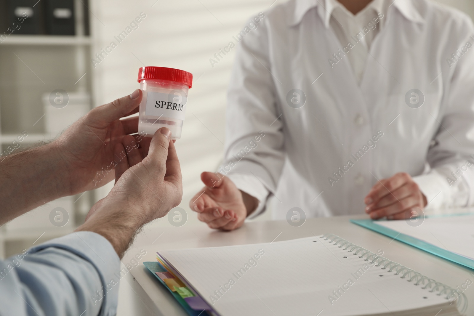 Photo of Donor giving container of sperm to doctor in hospital, closeup