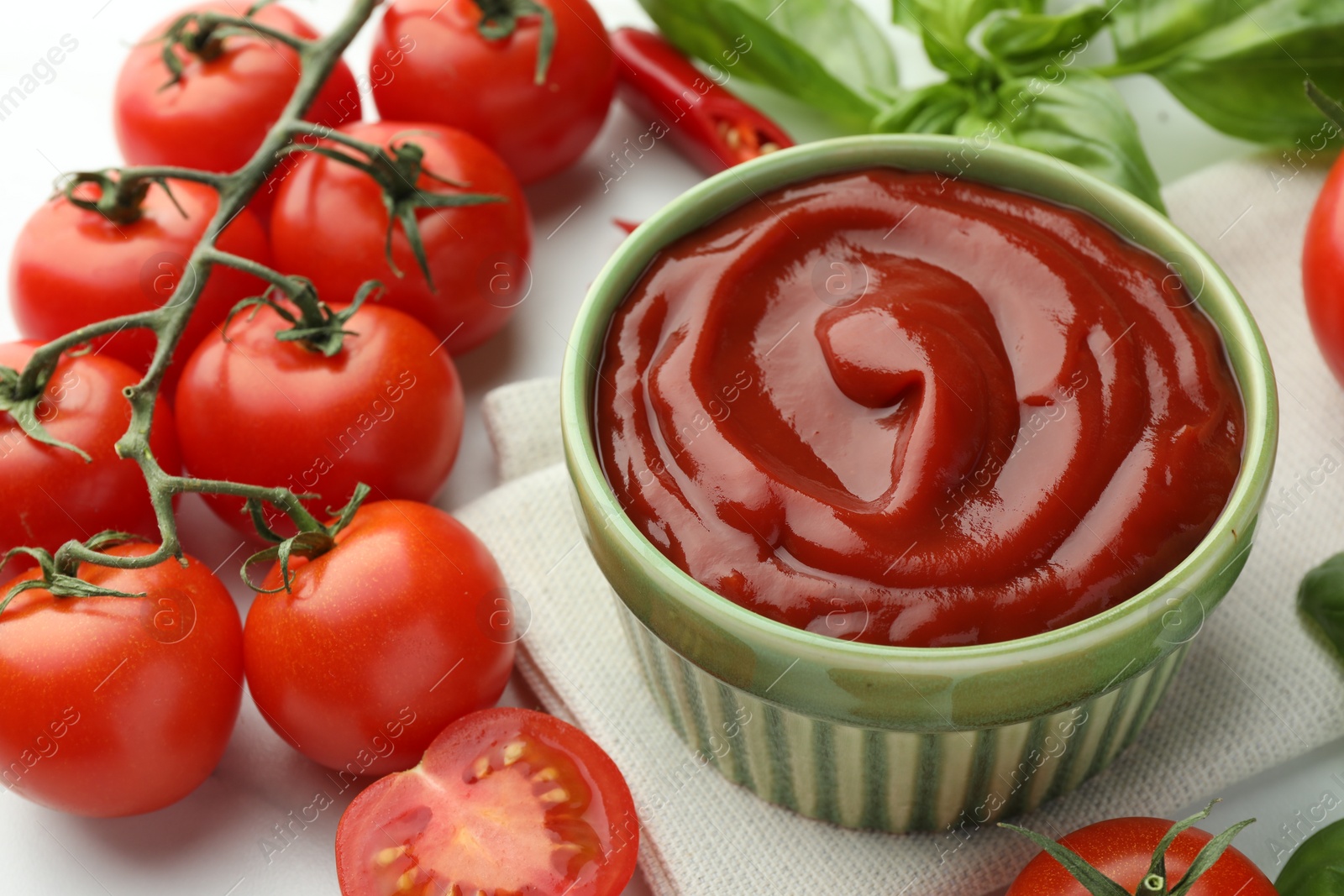 Photo of Bowl of tasty ketchup and ingredients on white table, closeup