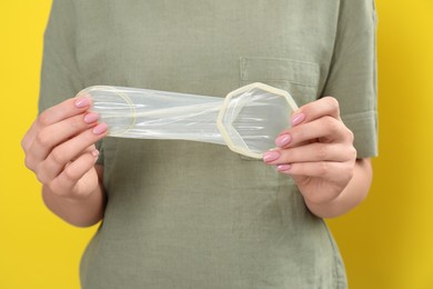 Woman with unrolled female condom on yellow background, closeup. Safe sex