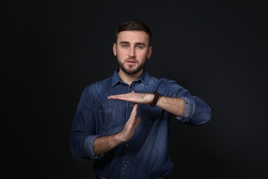 Photo of Man showing TIME OUT gesture in sign language on black background