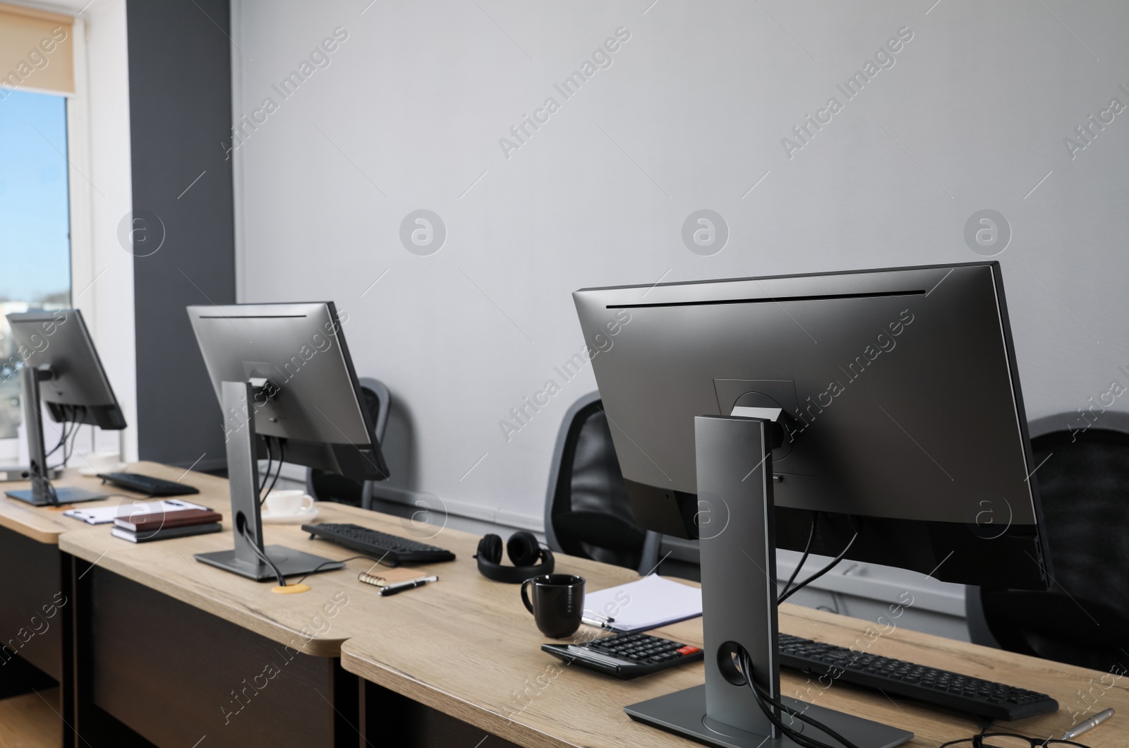 Photo of Open office interior. Modern workplaces with computers near light grey wall