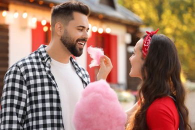 Photo of Young woman treating her boyfriend with cotton candy outdoors