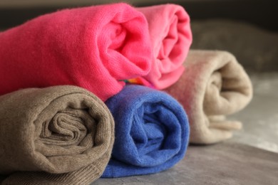 Photo of Rolled color sweaters on gray table, closeup