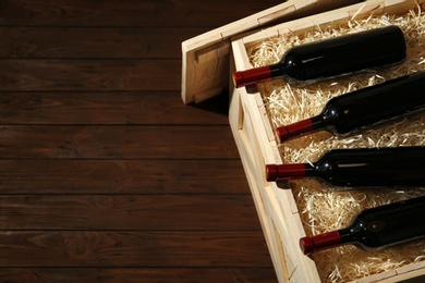 Photo of Crate with bottles of wine on wooden background. Space for text