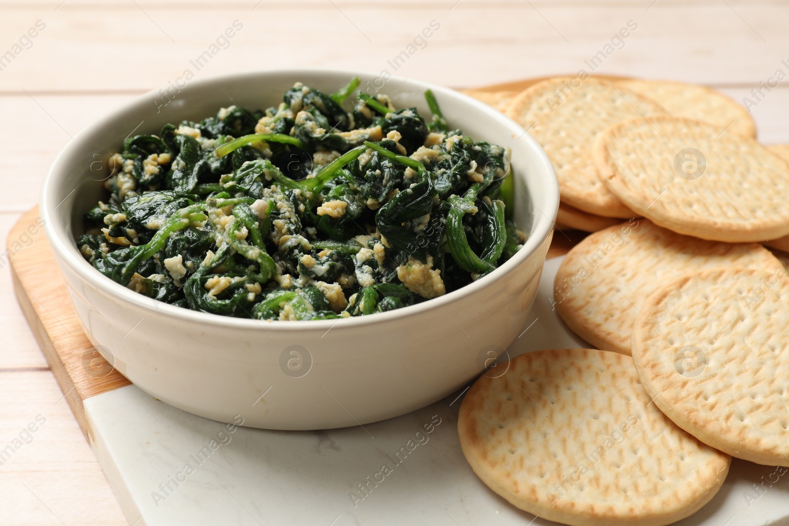 Photo of Tasty spinach dip with eggs in bowl and crackers on light wooden table, closeup