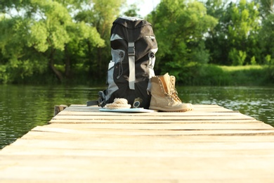 Photo of Backpack and camping equipment on wooden pier near river