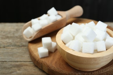 Photo of White sugar cubes in bowl and scoop on wooden table, closeup